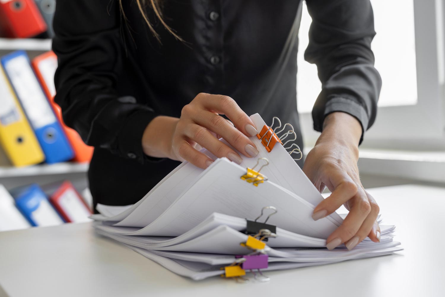 Person organising printed documents clipped together on an office desk.